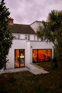 Rear view of a cottage with an extension, welcomingly lit from the inside