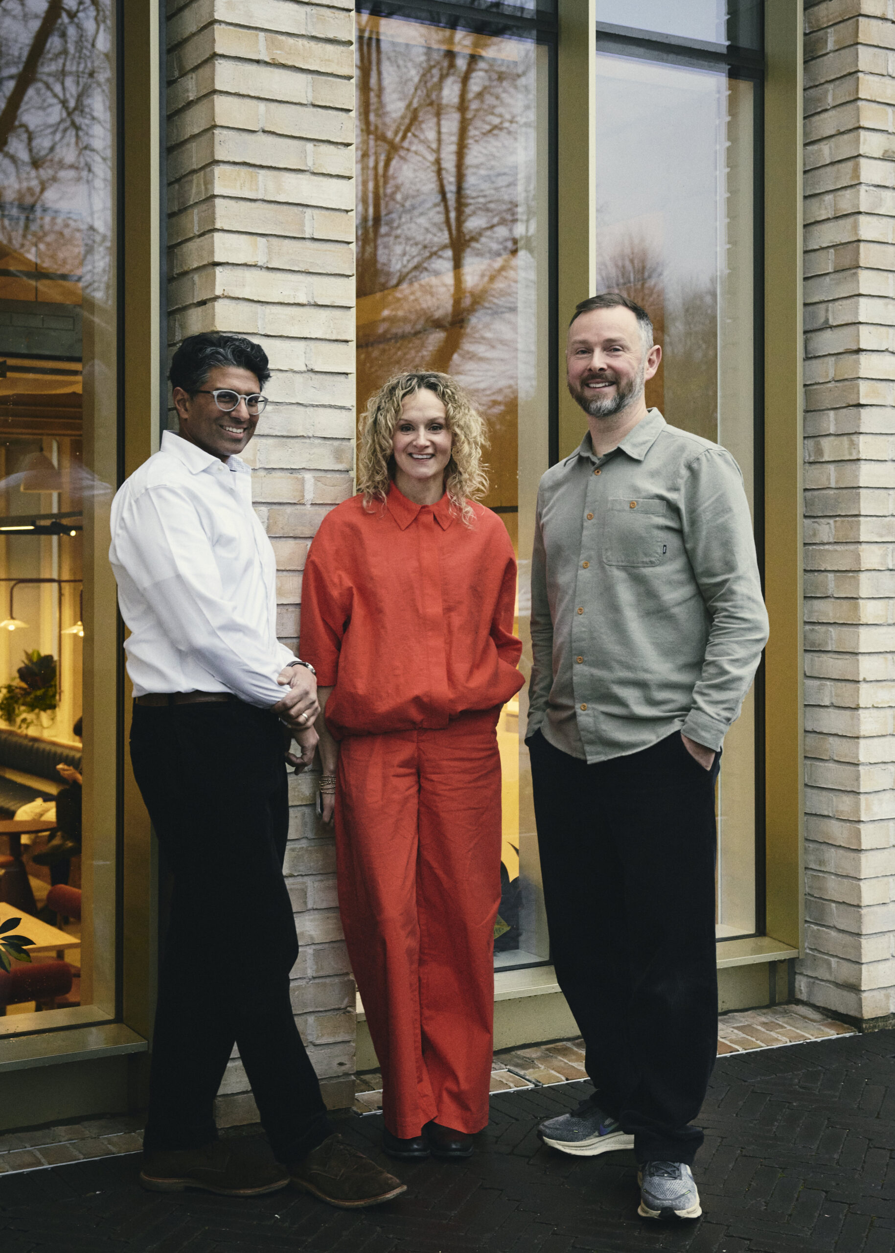 Three diverse people stand infront of a modern building.