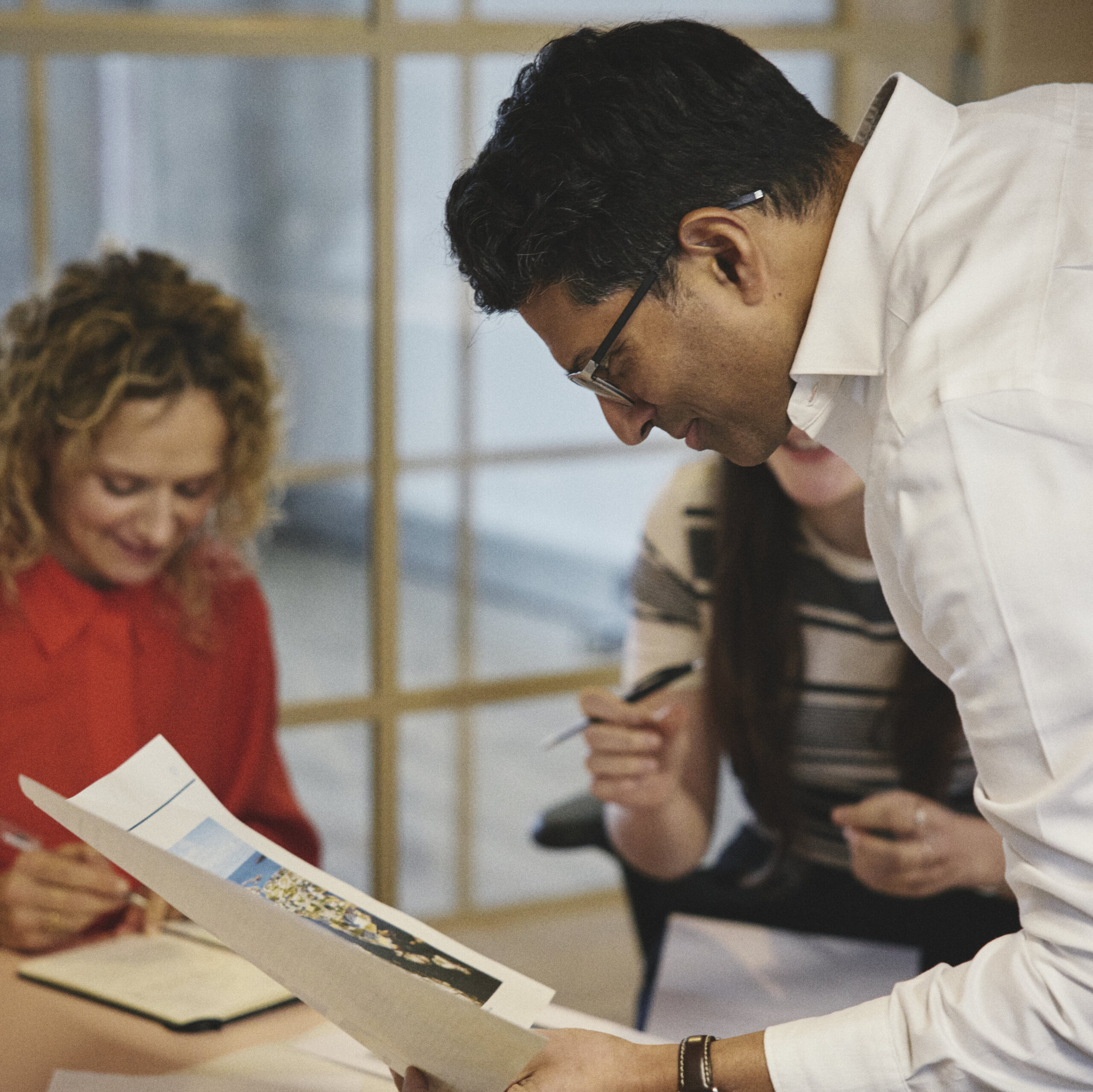 A creative meeting - a man leans over to look more closely at a drawing, two women sit and the table discussing the document
