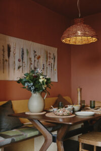 Above the dining table, an Abigail Ahern lampshade evokes the colour and texture of the home and a bespoke botanical wallhanging from brings wildflowers to the table.