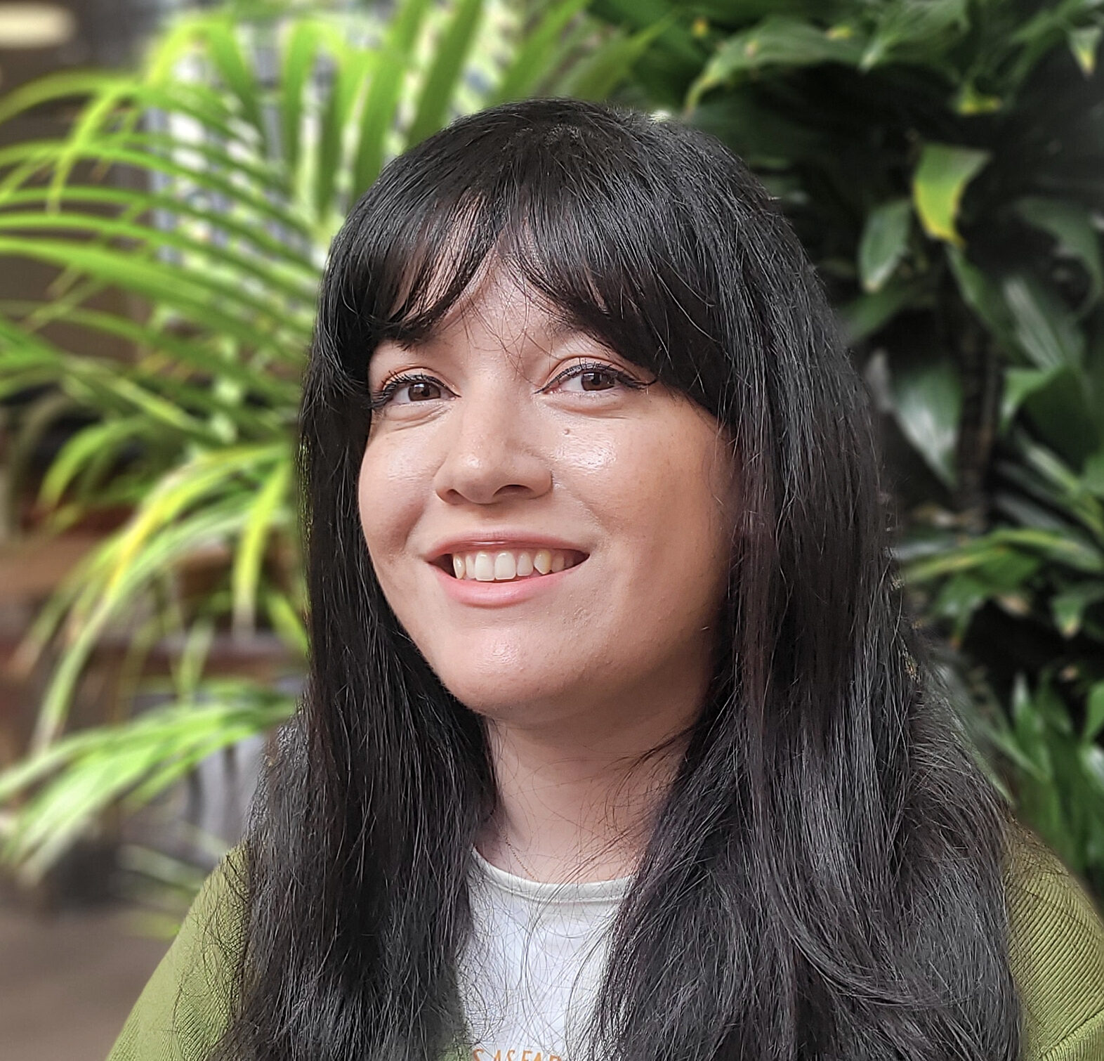 Head and shoulders of a young woman with dark hair. she sits in an office lobby environment